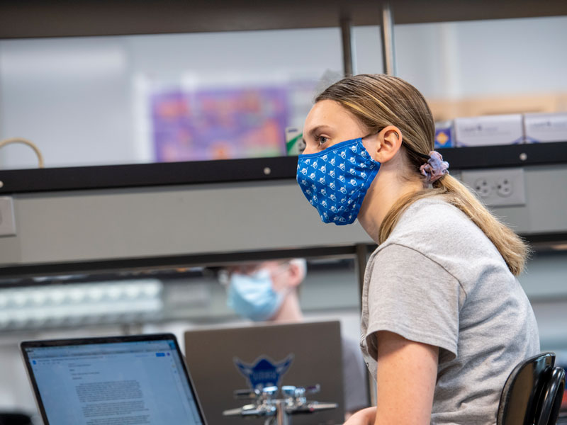 a female student with a mask looks up from a computer in a lab classroom