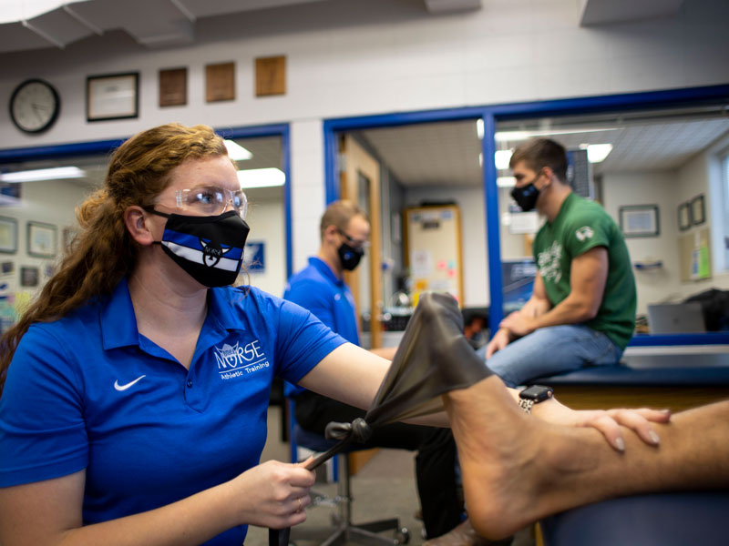 two athletic trainers assist two students with physical therapy exercises
