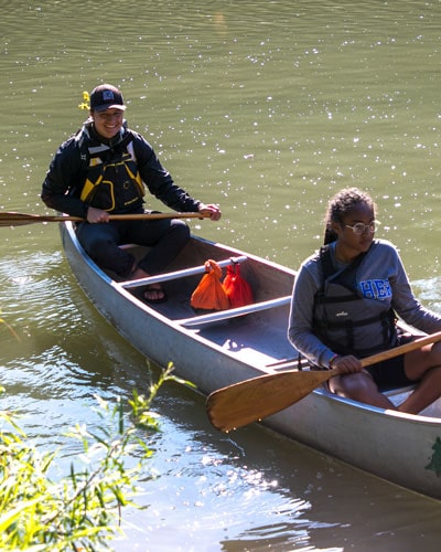two Luther students rowing a canoe down a river