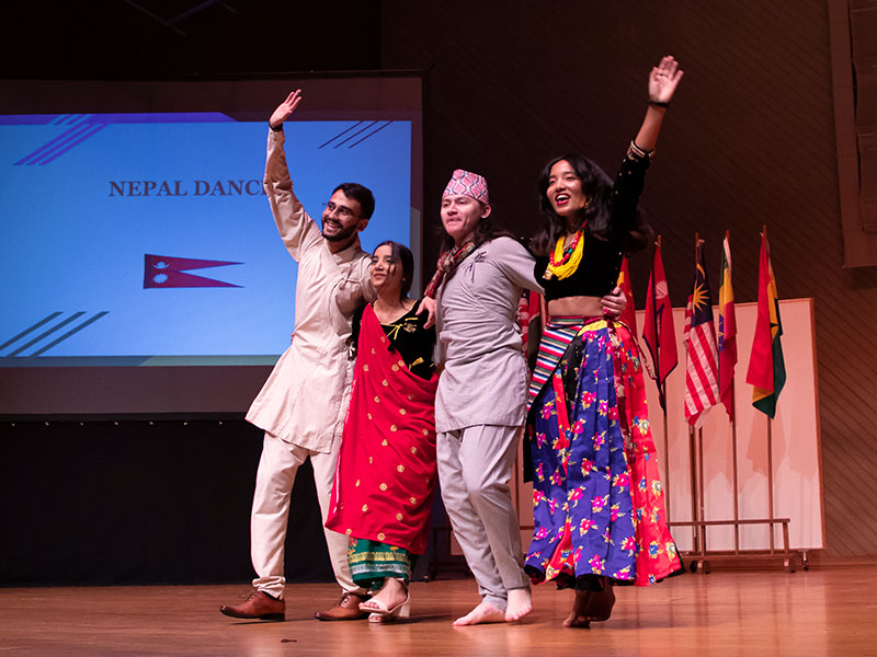 Four students from Nepal in traditional clothing walking onto the stage