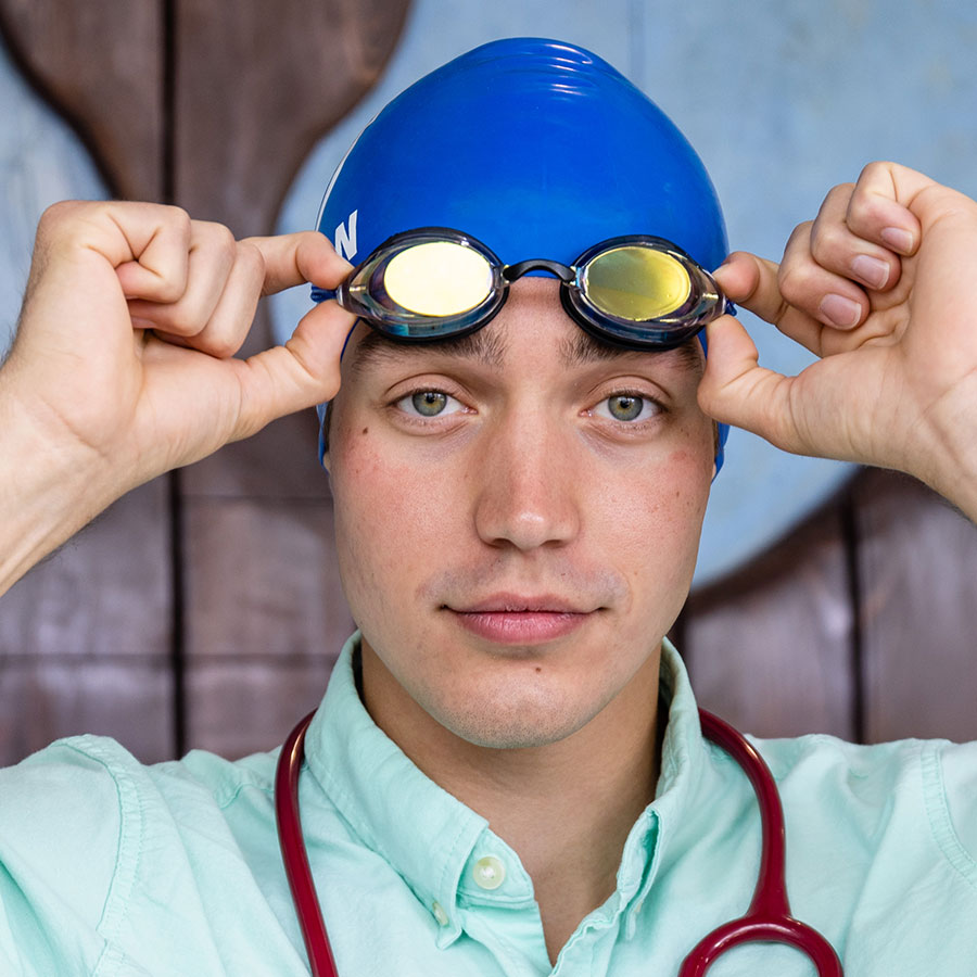 White man wearing swim cap with goggles, plus a stethoscope