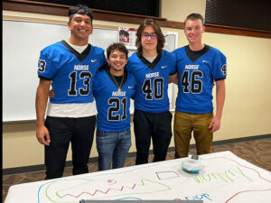 Photo of four Luther football players inside an elementary school
