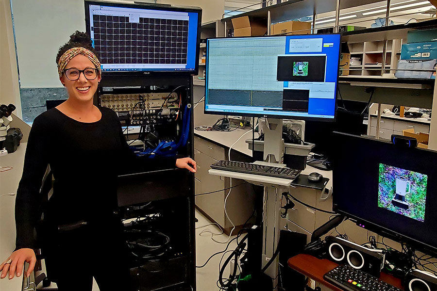 Neuroscientist Krista Wahlstrom standing in front of several computer monitors and other equipment