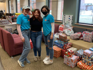 Photo of three Luther students standing near piles of wrapped Christmas presents