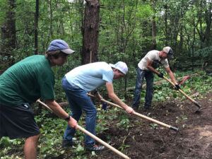 Photo of three Luther athletes working with hand tools to maintain a forested trails