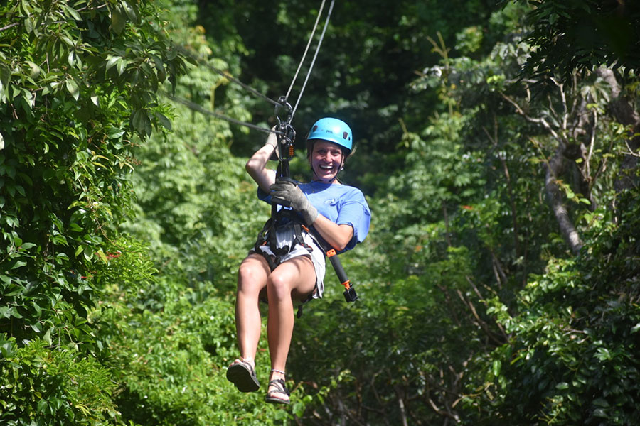 A smiling woman ziplining surrounded by foliage