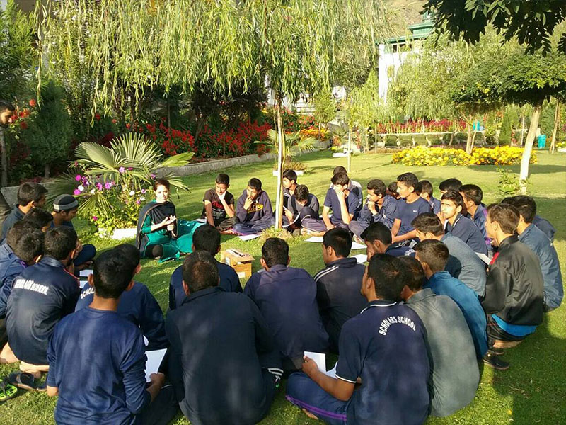 A group of about 30 people, all young men and one woman, seated in a circle outdoors