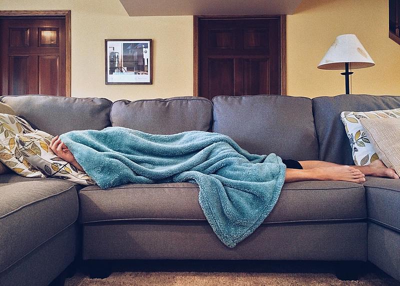 person sleeps under a blanket on couch