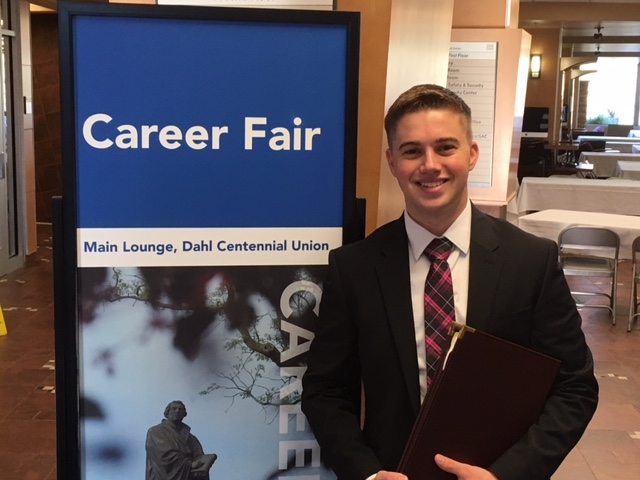 student stands in front of career fair banner