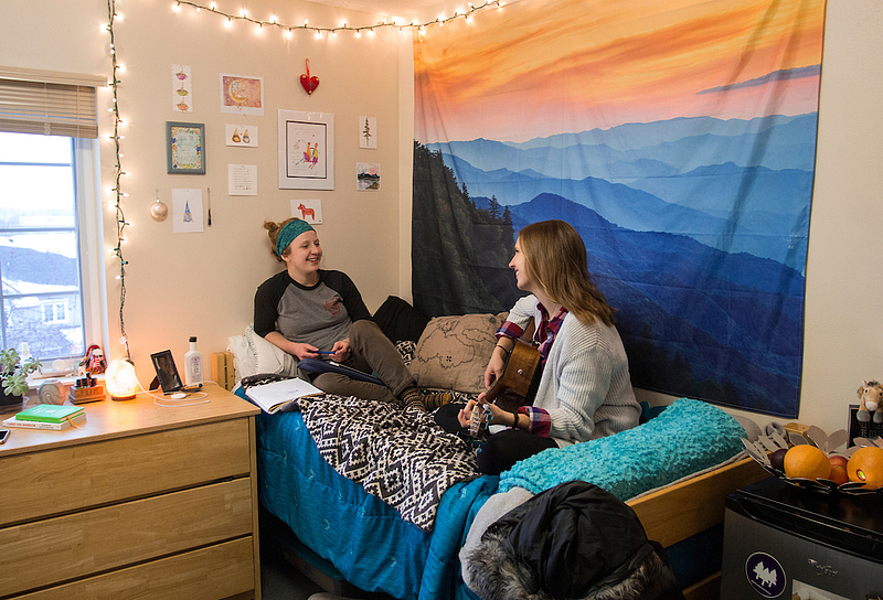students chat in their dorm as one holds a guitar