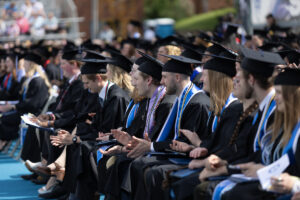 A group of students sitting in caps and gowns for graduation outdoors.